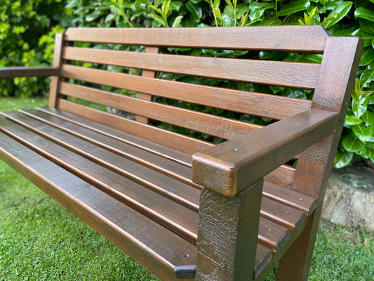 A dark oak finished garden bench situated on a lawn, showing the side profile with the backrest and seating area.