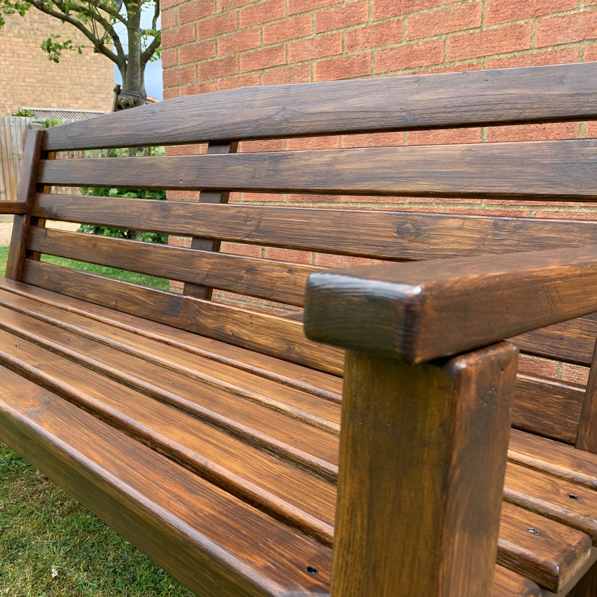 Handmade dark oak garden bench on lawn with brick building, Whaley Woodworks