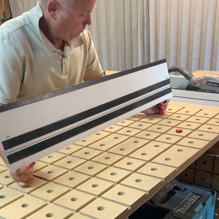 Woodworker positioning a track-saw guide rail over timber on a dog-hole workbench.
