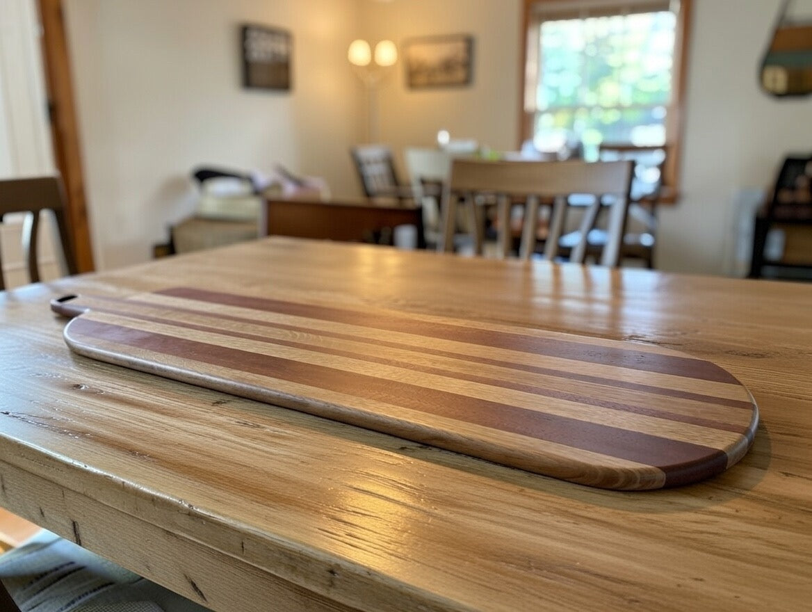 Handmade long hardwood charcuterie board with mixed wood stripe detail on a rustic dining table