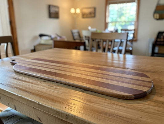 Handmade long hardwood charcuterie board with mixed wood stripe detail on a rustic dining table