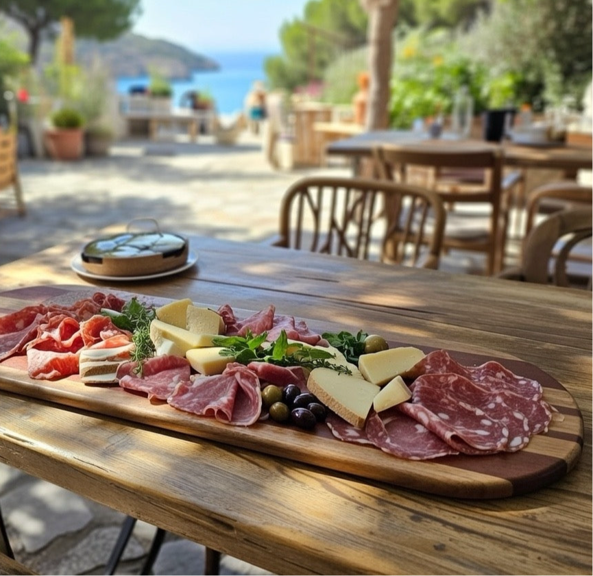 Handmade hardwood grazing board loaded with cured meats, cheese and olives shared outdoors
